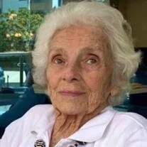 Elderly woman smiling in a white shirt indoors.