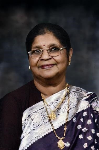 Smiling woman in sari with glasses and jewelry.