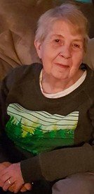 Elderly person sitting on a couch, smiling gently.