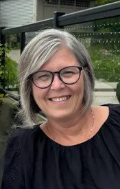 Smiling woman with glasses and gray hair outdoors.