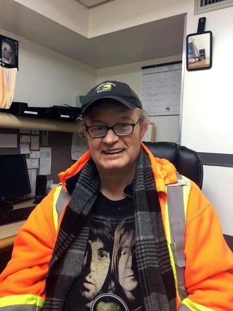 Smiling man in office wearing orange safety jacket.