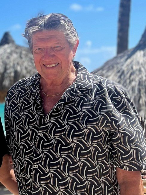 Smiling person in patterned shirt at tropical beach.