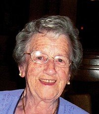 Elderly woman smiling, wearing glasses and a blue top.