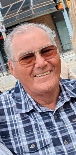 Smiling man in sunglasses and plaid shirt outdoors.