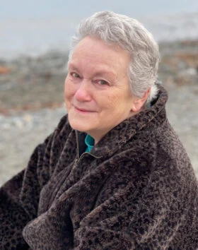 Elderly person in a fur coat, seated outdoors.