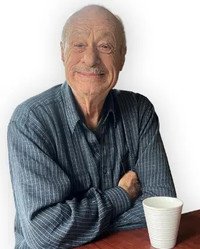 Smiling man with coffee cup, sitting at table.