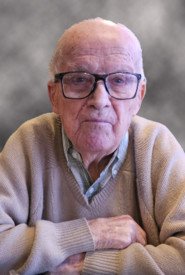 Elderly man wearing glasses and sweater, seated indoors.