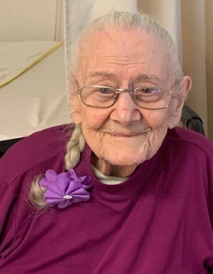 Elderly woman smiling with purple shirt and flower