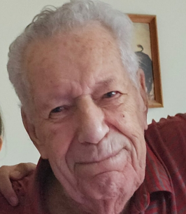 Elderly man smiling indoors with a painting behind.