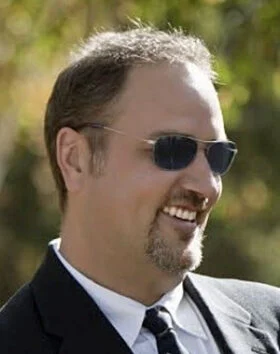 Man in suit, sunglasses, smiling outdoors