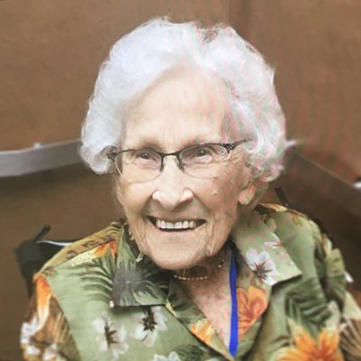 Smiling elderly woman with glasses wearing floral shirt.
