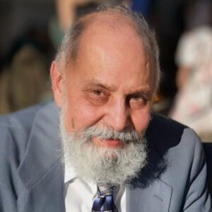 Elderly man in a suit smiling outdoors.