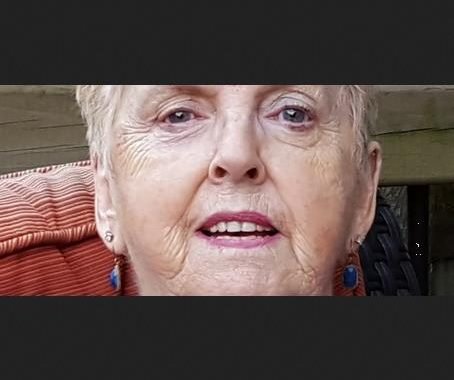 Older woman with earrings and short hair outdoors.
