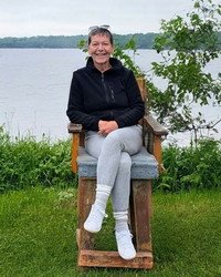 Person sitting on wooden chair by a lake.
