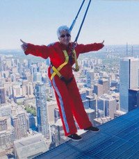 Person on skyscraper rooftop with harnessed arms outstretched.