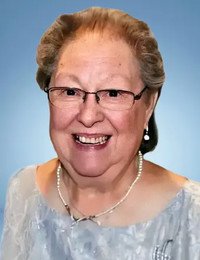 Smiling elderly woman wearing glasses and pearl necklace.