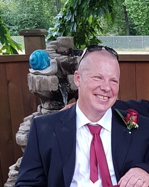 Smiling man in suit sitting by garden fountain.