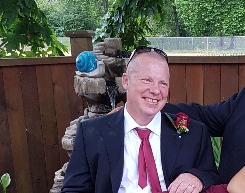 SORLAND, Barry James Sorland Smiling man in suit sitting by garden fountain.