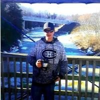 Man on a bridge with snowy river view.