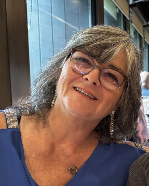 Smiling woman with gray hair and glasses indoors.