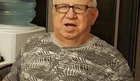 Elderly man in glasses and patterned shirt indoors.