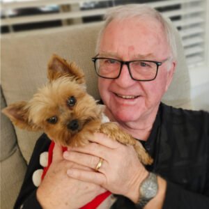 Man holding small dog, smiling indoors