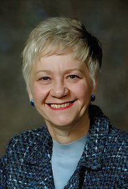 Smiling person with short hair in formal attire.