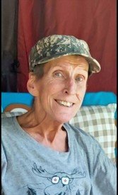 Smiling person wearing camouflage hat indoors.