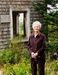 Person standing by rustic building and greenery.