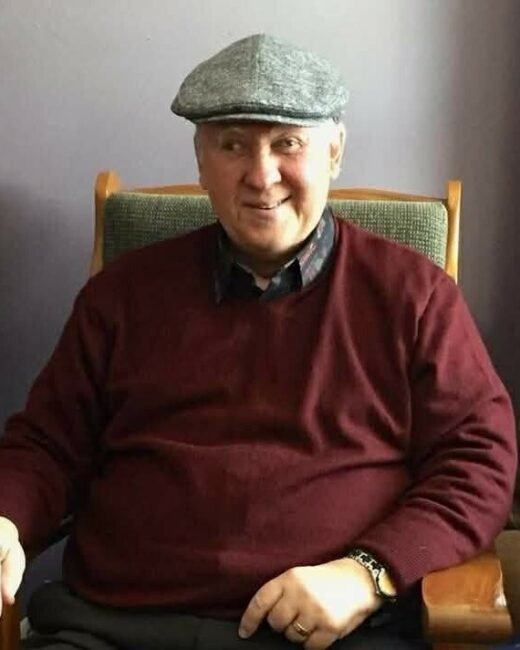 Smiling older man in a cap on chair.