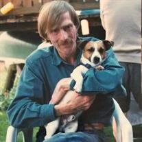 Man in blue shirt holding small dog outdoors.