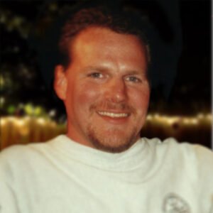Smiling man in outdoor setting at night.