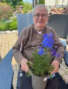 Elderly man holding potted purple flowers