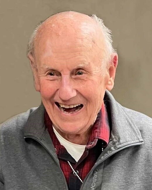 Elderly man smiling in gray jacket.