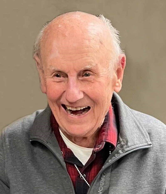 Elderly man smiling in gray jacket.