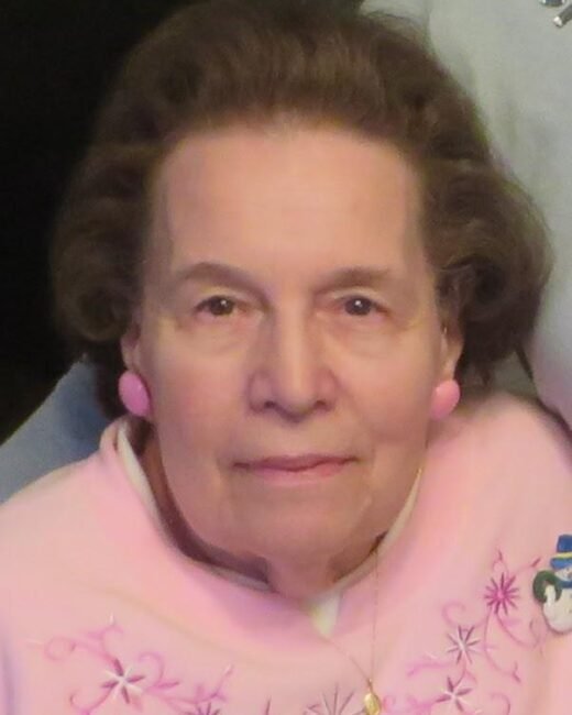 Elderly woman wearing pink sweater with floral embroidery.