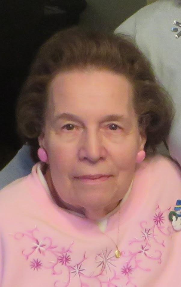 Elderly woman wearing pink sweater with floral embroidery.