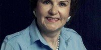 Smiling woman in blue blouse and necklace.