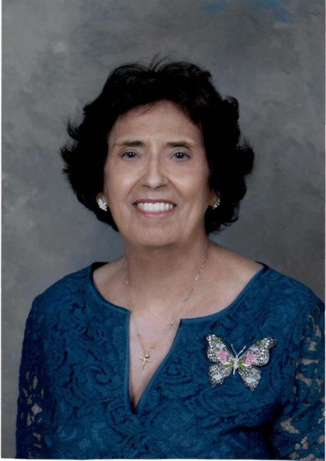 Smiling woman in blue dress with butterfly pin.