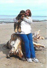 Person with dog sitting on beach driftwood.