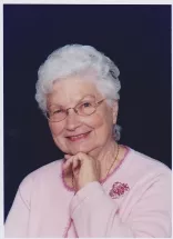 Elderly woman smiling in pink sweater and glasses.