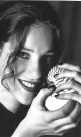Woman smiling, holding seashell to face