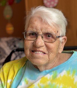 Elderly woman smiling with glasses, tie-dye shirt.