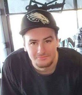 Man in Eagles cap and black shirt indoors.