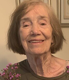 Smiling elderly woman holding small purple flowers.