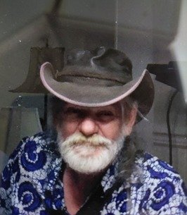 Man in cowboy hat with patterned shirt smiling.