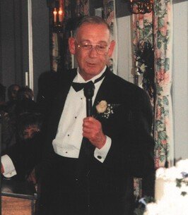 Elderly man in tuxedo speaking at event.