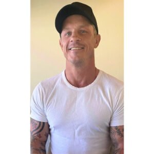 Man smiling, wearing white shirt and black cap.