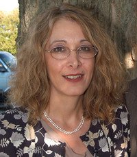 Smiling person outdoors with glasses and curly hair.