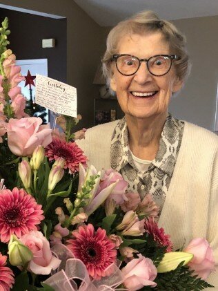 Smiling elderly woman with bouquet of pink flowers.